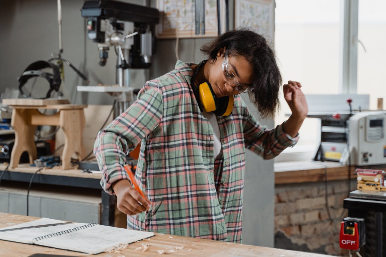 A skilled woman crafting at a woodworking workshop, using tools and taking notes.