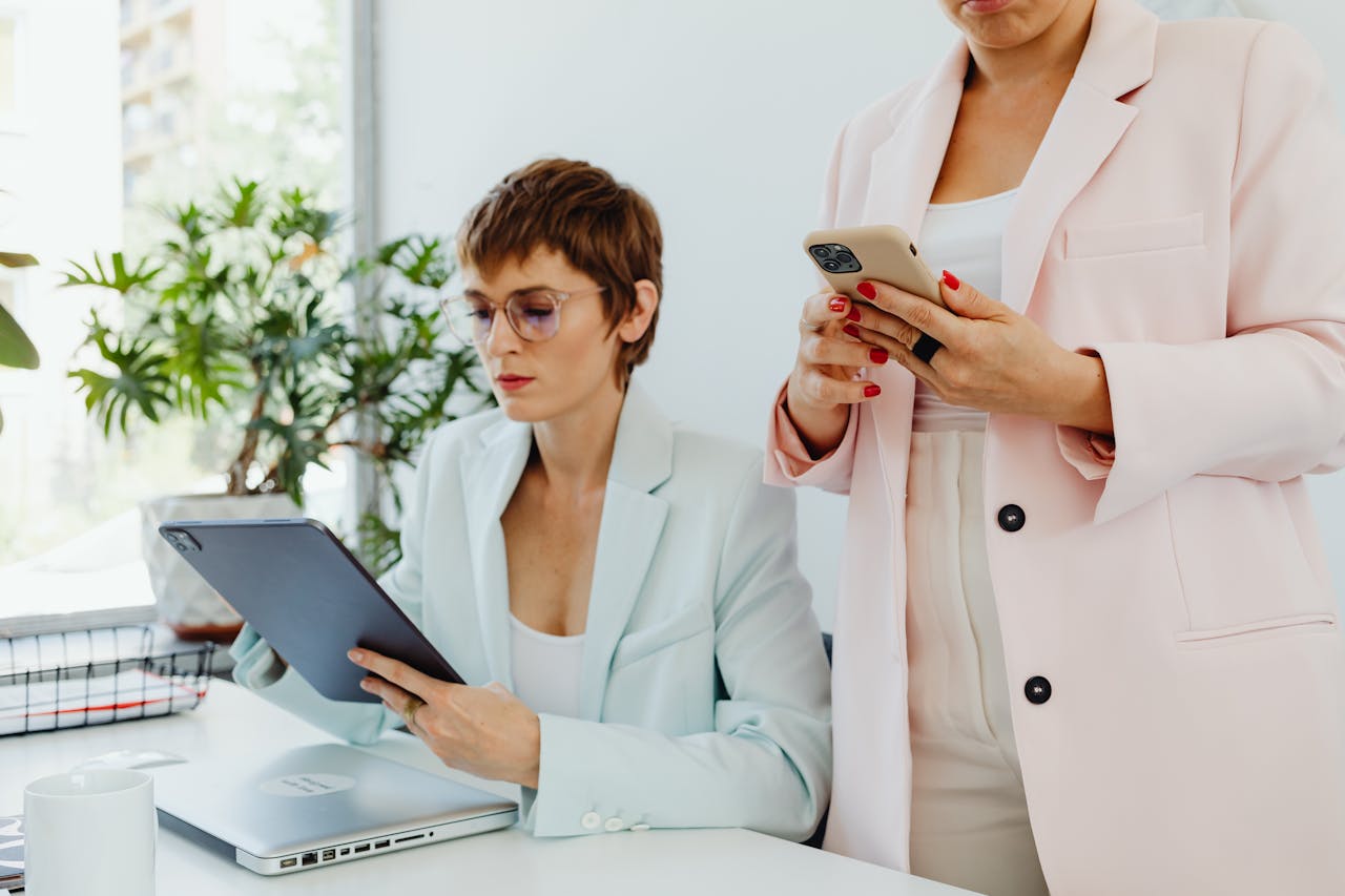 Two businesswomen using tech devices in a modern office setting.